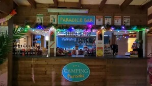 A wooden bar area with a sign reading 'PARADISE BAR' and another sign below it stating 'CAMPING Paradise.'