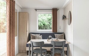 A compact room with a window, a table with chairs, a bench, and a door. - Camping 4 étoiles - Piscine  - ccbg0fc (Saint-Christophe-du-Ligneron)