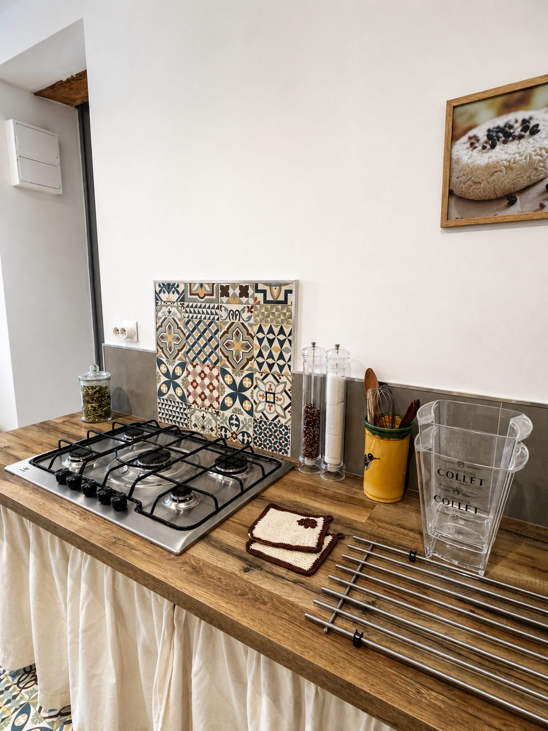Una cocina con estufa a gas, salpicadero decorado, tarro de especias, recipiente amarillo con utensilios y jarra de vidrio.