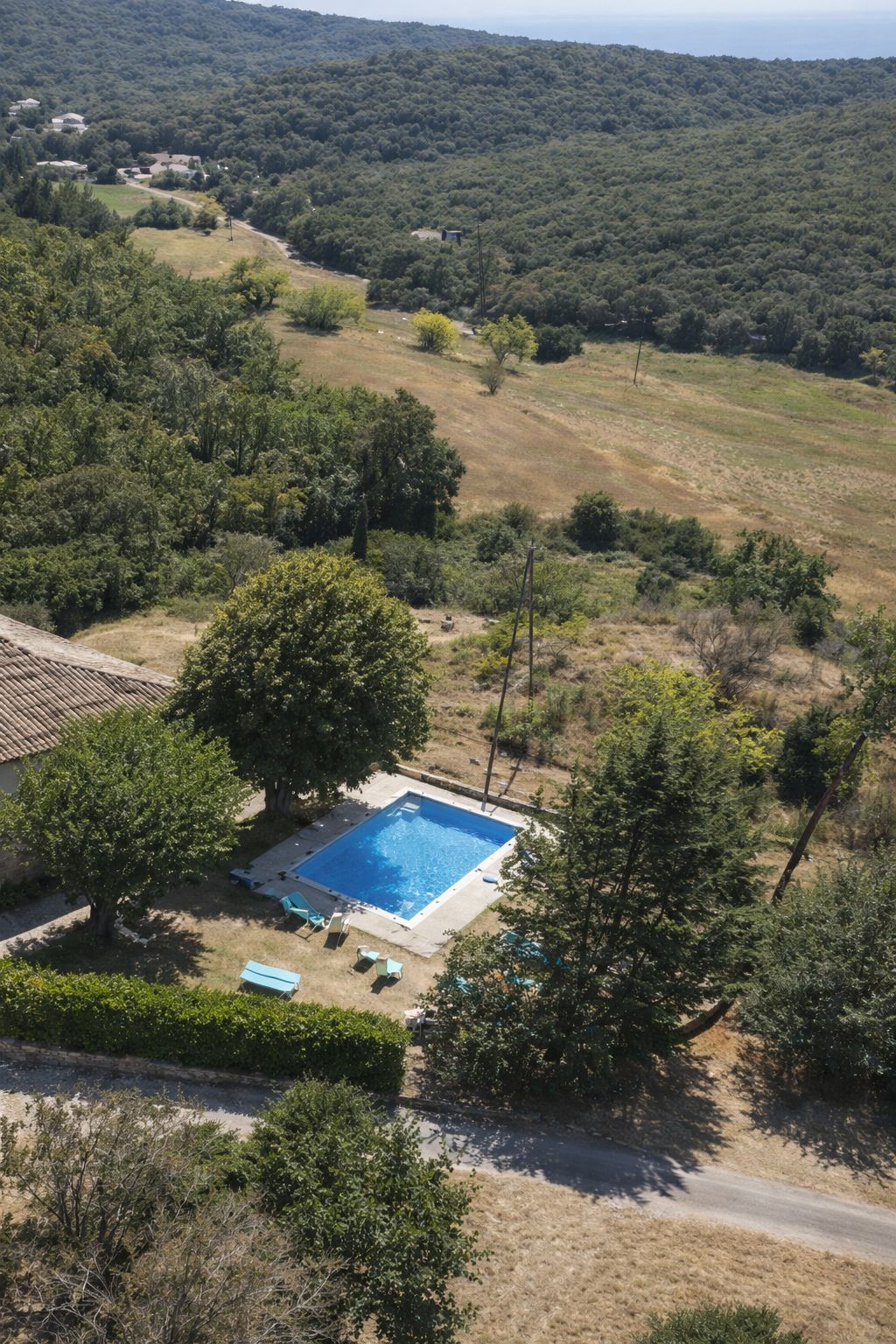 Una piscina cuadrada rodeada de árboles, con una carretera y casas al fondo.