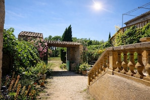 A garden pathway leading to a stone building with a tiled roof, surrounded by lush greenery and flowering plants. - Fig Trees · Panoramic View and Pool (Saint Montan)