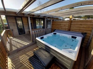 Eine Holzterrasse mit Whirlpool, überdachter Sitzgelegenheit und Holzlattenzaun.