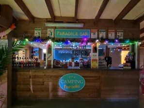 Eine Holztresore mit einem Schild, auf dem 'PARADISE BAR' steht, und darunter ein Schild mit der Aufschrift 'CAMPING Paradise'.
