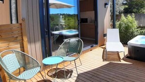 Una terraza moderna al aire libre con un jacuzzi, una mesa con sillas y una puerta corrediza de vidrio que da a una habitación.