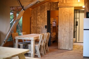 A wooden interior with a dining table and chairs, a wooden door, and a white refrigerator. - Camping 2 étoiles - Piscine  - ccbfiig (Villeneuve-lès-Avignon)