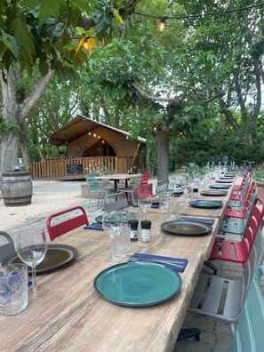 An outdoor dining area with tables set for a meal, surrounded by trees and a wooden structure. - Camping 2 étoiles - Piscine  - ccbfiig (Villeneuve-lès-Avignon)