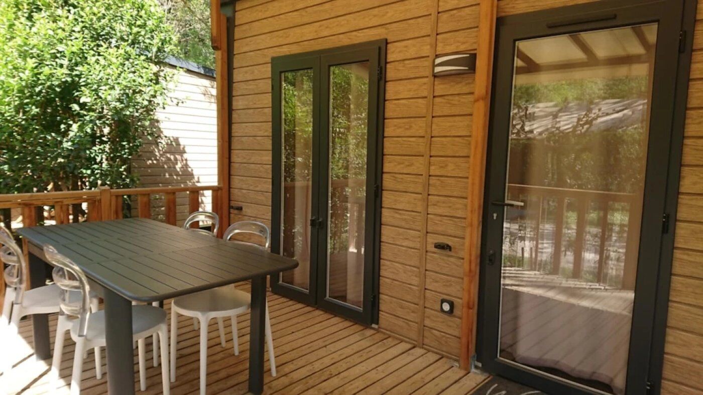 Una terraza de madera con una mesa y sillas, una puerta corrediza de vidrio y vistas al exterior.