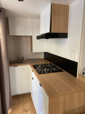 A compact kitchen with white cabinets, a black stove, and a wooden countertop. - Camping 2 étoiles - Piscine  - ccbfiii (Villeneuve-lès-Avignon)