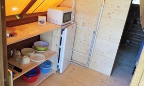 Et kompakt køkken med mikrobølgeovn, køleskab og hylder af træ.