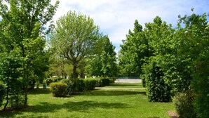 A well-maintained garden with various trees and shrubs, a clear sky, and a pathway leading to a building. - Camping 3 étoiles - Piscine  - ccbgaad (Mens)
