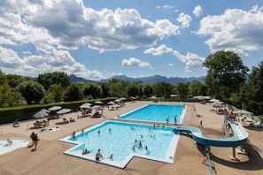 Un área de piscina con varias piscinas, sillas de descanso y sombrillas.