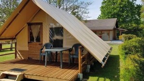 A single-story wooden structure with a slanted roof, a small porch with a table and chairs, and a covered outdoor seating area. - Camping 3 étoiles - Piscine  - ccbgaad (Mens)