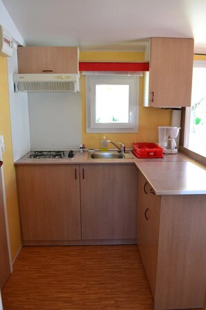 Een kleine keuken met een gasfornuis, spoelbak en een raam boven het aanrecht.