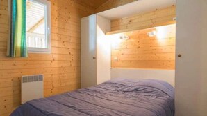 Et soveværelse med trævægge, en seng, et vindue med gardiner og en loftlampe.
