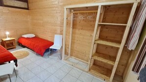 Una habitación de madera con dos camas, una silla blanca, una mesita de noche y un armario de madera.