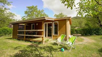 Eine Holzhütte mit Veranda, überdachter Sitzgelegenheit und zwei Liegestühlen.