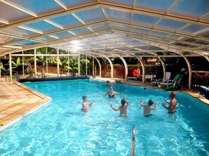 Une piscine intérieure dotée d’un toit en verre, entourée de chaises longues et d’une terrasse en bois.
