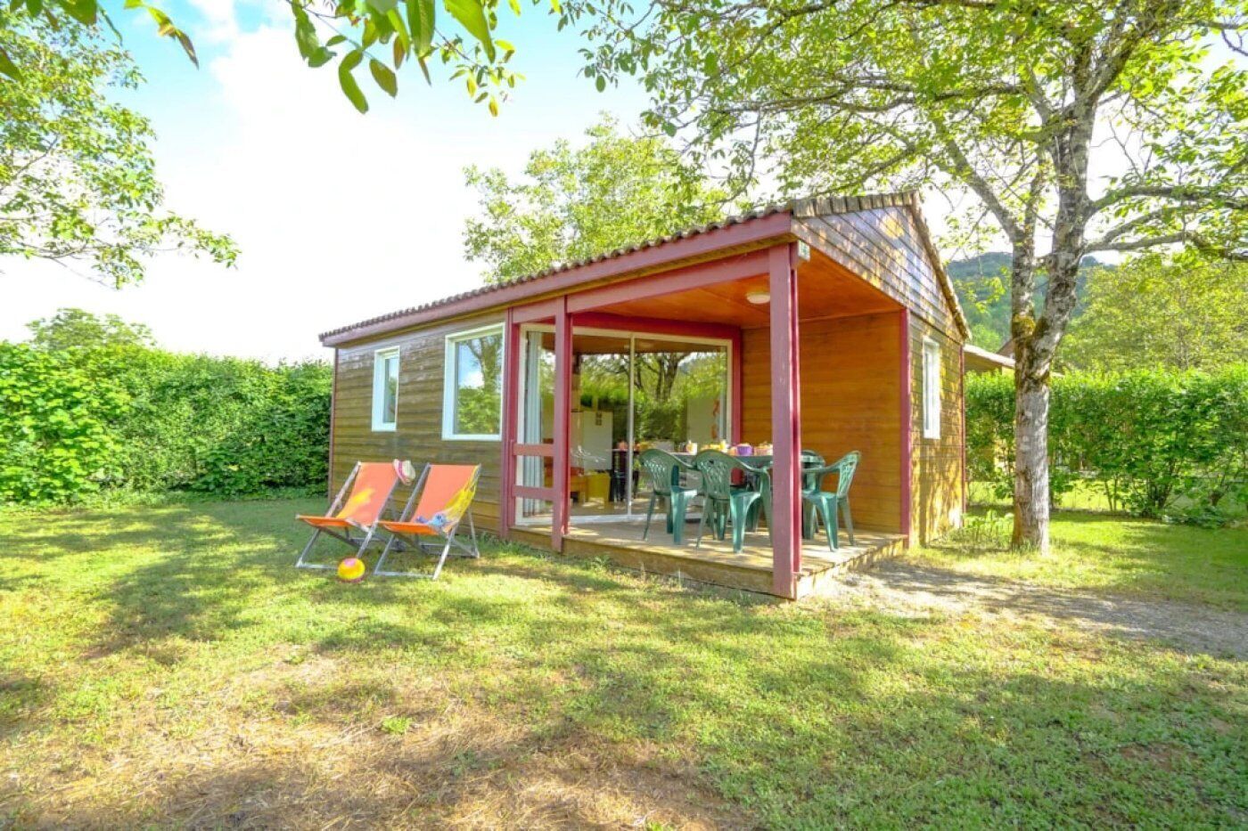A small wooden cabin with a covered patio, two lounge chairs, and a table.