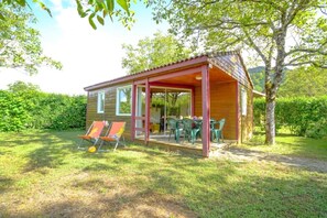 Eine kleine Holzhütte mit einer überdachten Veranda, zwei Liegestühlen und einem Tisch.