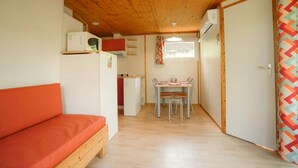 Habitación pequeña con techo de madera, una kitchenette, un rincón de comedor con mesa y sillas, y una cama individual.