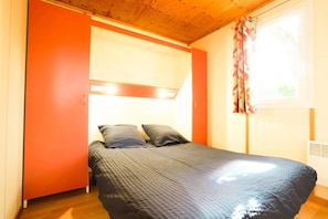 Een slaapkamer met een bed, een raam met gordijnen en een houten plafond.
