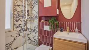 Ein Badezimmer mit Duschkabine aus Glas, Marmorwand, roter Fliesenrückwand, Waschtisch aus Holz und einem großen Spiegel.