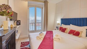 Ein Hotelzimmer mit Bett, einem Fenster mit Vorhängen, einem Nachttisch mit Lampe und Blick auf die Stadt.