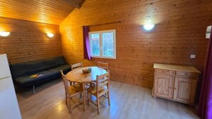 Interior de uma cabana de madeira com uma mesa de jantar, cadeiras, um sofá, uma janela e um armário.