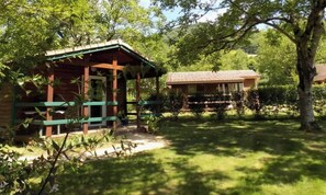 Une cabane en bois dotée d’un porche, entourée d’une végétation luxuriante et d’arbres.