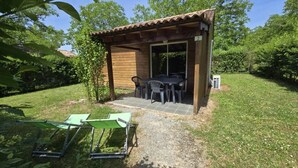 Um alpendre de madeira ao ar livre com mesa e cadeiras, um espaço coberto para sentar e um pequeno jardim.