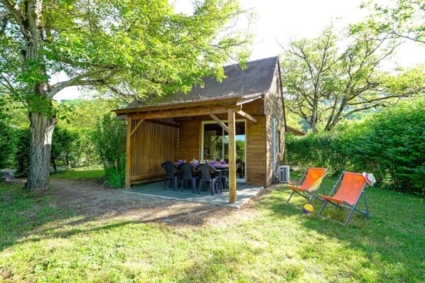Un pavillon en bois, avec une table et des chaises, entouré de verdure.