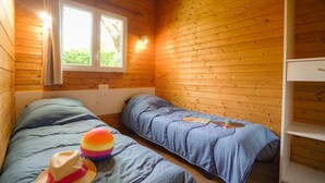 Ein Blockhauszimmer mit zwei Betten, einem Fenster und einem weißen Regal.