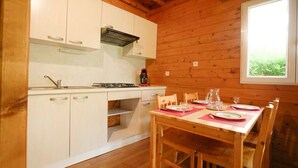 Ein Interieur einer Holzhütte mit Küche und Essbereich, ausgestattet mit Schränken, einem Herd und einem für das Essen gedeckten Tisch.