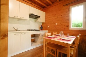 Puinen mökki, jonka sisätiloissa on keittiö ja ruokailutila. Keittiössä on kaappeja, liesi ja ruokapöytä, joka on katettu.