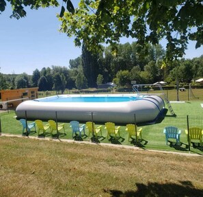 Ein rechteckiger aufblasbarer Pool mit einer Leiter, umzäunt und mit mehreren Stühlen drumherum.