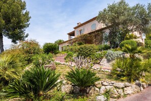 Eine mediterrane Villa mit einer Steintreppe, die zum Eingang führt, umgeben von üppiger Vegetation und verschiedenen Pflanzen.
