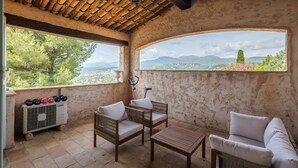 Un espacio de estar techado al aire libre con mobiliario de mimbre, una mesa y vistas del paisaje.