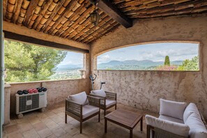 Ein überdachter Sitzbereich im Freien mit Korbmöbeln, einem Tisch und Blick auf die Landschaft.