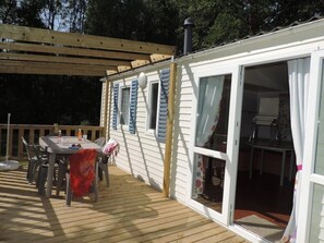 Eine Holzterrasse mit Tisch und Stühlen, ein überdachter Bereich mit Tisch sowie eine Glastür zu einem Innenraum.