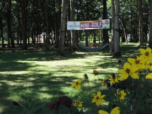Schild für 'MINI-GOLF' in einem Park mit Bäumen und einer Hängematte.