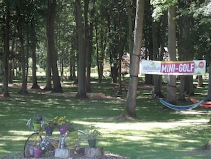 Schild für einen Minigolfplatz in einer bewaldeten Gegend mit einem Fahrrad und Topfpflanzen.