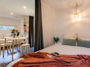 Ein modernes Schlafzimmer mit einem Bett, einem Schreibtisch, Stühlen und einem kleinen Tisch mit Blumen in einer Vase.