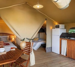 Ein kleines Zimmer mit Bett, Tisch, Stuhl, einer Küchenzeile und einem Deckenventilator.