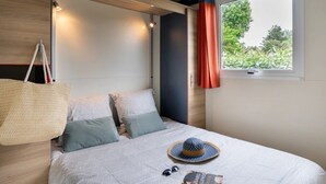 Una cama con ropa de cama estampada, un sombrero, gafas de sol y un libro encima.