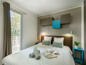 Ein Hotelzimmer mit Bett, Nachttisch, Topfpflanze und Blick ins Freie.