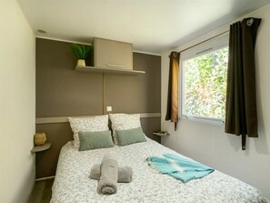 Ein Schlafzimmer mit Bett, Kissen, einem Nachttisch, einer hängenden Pflanze und einem Fenster mit Vorhängen.