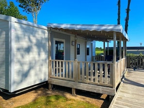 Eine kleine, eingeschossige Hütte mit Veranda und einem umzäunten Deckbereich.