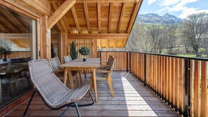 Una terraza de madera con una mesa, sillas, un vidrio y vistas a montañas.