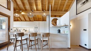 Una cocina moderna con vigas de madera, luces colgantes y una isla central con taburetes de bar.