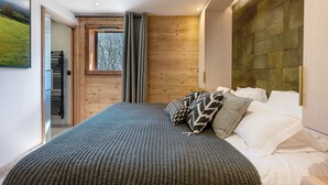Un dormitorio con una cama grande, cabecera de madera, ventana con cortinas y vistas a un paisaje verde.